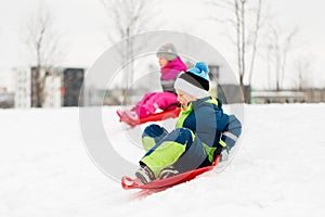 Kids sliding on sleds down snow hill in winter