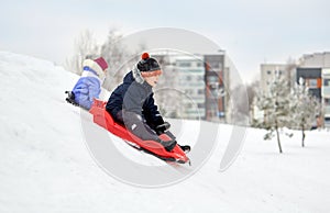 Kids sliding on sleds down snow hill in winter