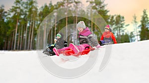 Kids sliding on sleds down snow hill in winter