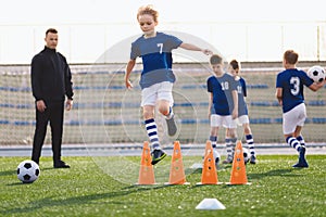 Kids on sports soccer training. Boys running balls and jumping over cones. Agility exercises for youths in football team