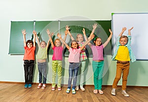 Kids stand with arms up in line near blackboard