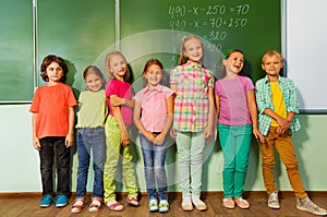 Kids stand in line near the blackboard and smile