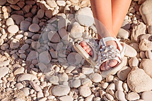 Kids summer sandals. baby shoes on stones beach. girl white fashion footwear, leather sandal ,moccasins.legs of