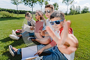 Kids in sunglasses reading books and one boy gesturing at camera