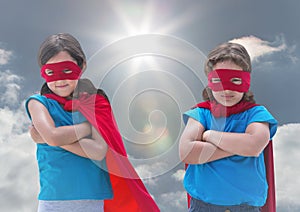 Kids in superhero costumes standing with arms crossed against sky in background