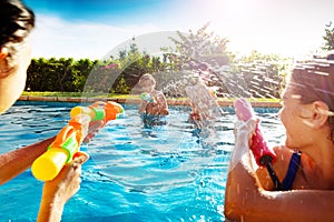 Kids in swimming pool shooting water squirt pistol