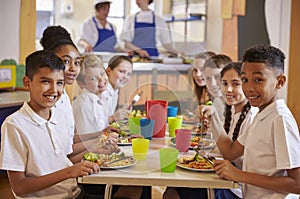 Kids at a table in a primary school cafeteria look to camera