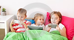 Kids with tablet pc and smartphones in bed at home