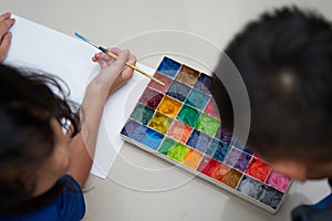 Kids together hold brush and plain paper with square color palette  for art work,top view
