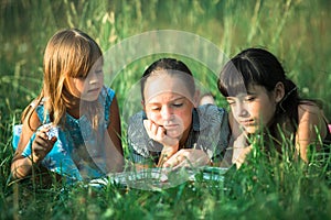 Kids together reading book in the green grass.