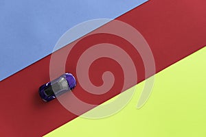 Kids toy car on trendy colorful background. Baby car top view on blue red yellow colored paper. Boys game. Travel and