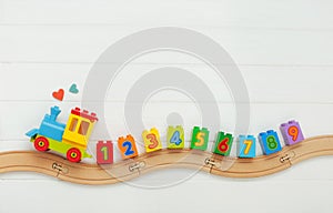 Kids toy train with numbers on railway on white wooden background with copy space