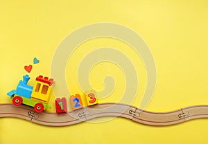 Kids toy train with numbers on toy wooden railway on yellow background with copy space