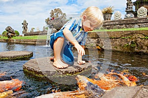 Kids walk by stepping stones, feeding koi fishes in pond