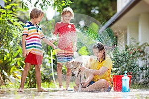 Kids wash dog in summer garden. Water hose fun