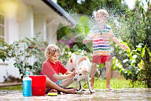 Kids wash dog in summer garden. Water hose fun