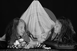 Kids wearing red jammies in bed on black background. Friends having fun with teddy bears in blanket tent