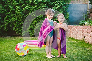 Kids wipes with towel after swimming in home inflatable pool. Brother and sister giggling wrapped in beach towels in the courtyard