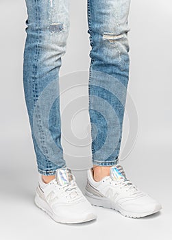 Kiev, Ukraine - January 03, 2021: White women`s casual sneakers from New Balance brand on a light background. Young girl in jeans