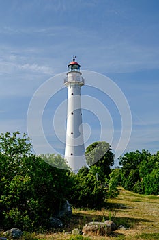 Kihnu island lighthouse in Estonia. Stand alone single white lighthouse stones green forest summer blue sky photo