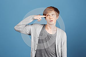 Kill me please. Young good-looking tired male student with ginger hair in casual gray outfit making gun gesture with
