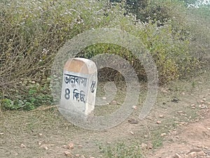 Kilometre Stone beside a rural Indian road with destination name Bengali word Bhalobasa written on it