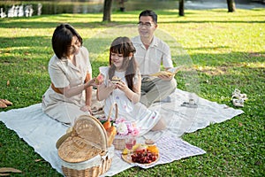 Kind Asian grandparents are enjoying a picnic in the garden with their adorable young granddaughter