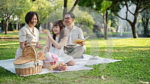 Kind Asian grandparents are enjoying a picnic in the garden with their adorable young granddaughter