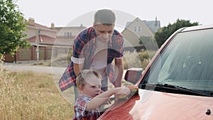 Kind caucasian dad patiently shows his son how to wash the car`s hood slow motion