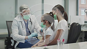 A kind doctor in protective glasses and a mask has given the child a girl a shot in the arm and nods approvingly to her