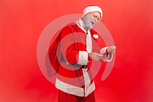 Kind gray bearded santa claus with big red bag reading letters with presents requests and greeting cards, magic of winter holidays