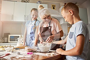 Kind-hearted grandma making cookies with her cute grandchildren