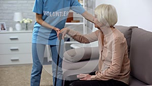 Kind hospital volunteer helping disabled pensioner with walking stick, altruism