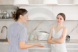 Kind middle-aged mother talking to young daughter in the kitchen