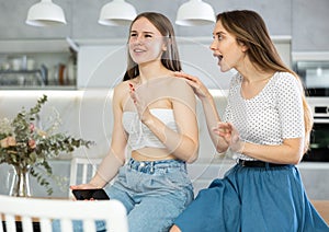 Kind middle-aged mother talking to young daughter sitting on kitchen-table