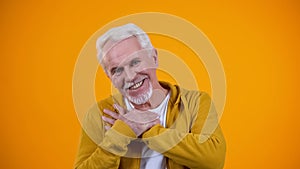 Kind old person crossing palms on breast, smiling to camera, sincerity concept