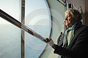 A kind old woman looks thoughtfully at the sea through the porthole of the ferry. Concept: solitude, recollection Caring
