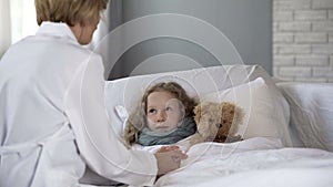 Kind pediatrician examining sick little girl at home, doctor comforting ill kid