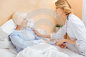 Kind responsible doctor persuading her senior patient to stay in bed