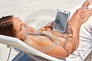 This kind of surfing is relaxing. a young woman using her tablet while relaxing at the beach.