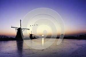 Kinderdijk - Geese flying over sunrise on the frozen windmills alignment