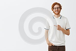 Kindly showing us great offer. Portrait of friendly and happy handsome redhead male model in white polo shirt pointing