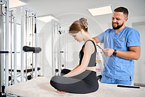 Kinesiologist glues black tape to the back of a patient