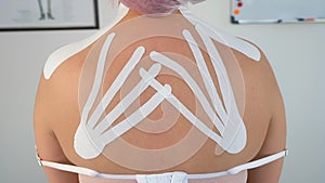 Kinesiology tapes on woman's back for fixation of muscles, closeup back view.