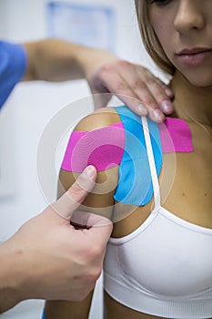 Kinesiology taping treatment with blue and pink tape on athlete patient injured arm. Young woman hands apply kinesio treatment