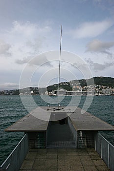 Kinetic sculpture of Eater Whirler on coastal deck with catwalk, and city on island across bay, Wellington, New Zealand