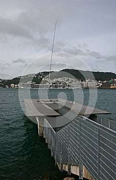 Kinetic sculpture of Eater Whirler on coastal deck with stairs and catwalk, and city on island across bay, Wellington, New Zealand