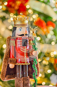 A king with a crown and cape  nutcracker stands  in front of  a  soft focused decorated Christmas tree