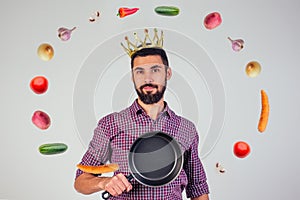 King of the kitchen with a golden crown on head chef holding a frying pan wizard man is cooking magic flying food salad