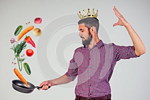 King of the kitchen with a golden crown on head chef holding a frying pan wizard man is cooking magic flying food salad
